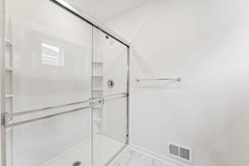 The owner's oversized shower includes shampoo shelves and sleek glass slider door. Similar home shown, Color and options can vary.