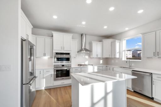 (Photo of a decorated model, actual homes finishes will vary) This stunning kitchen features a large center island, quartz countertops, LVP floors, stainless steel appliances, and more!