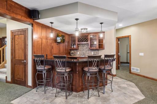 Custom pub style wrap around lower-level bar is built for entertaining and features rich wood cabinetry, and generous seating