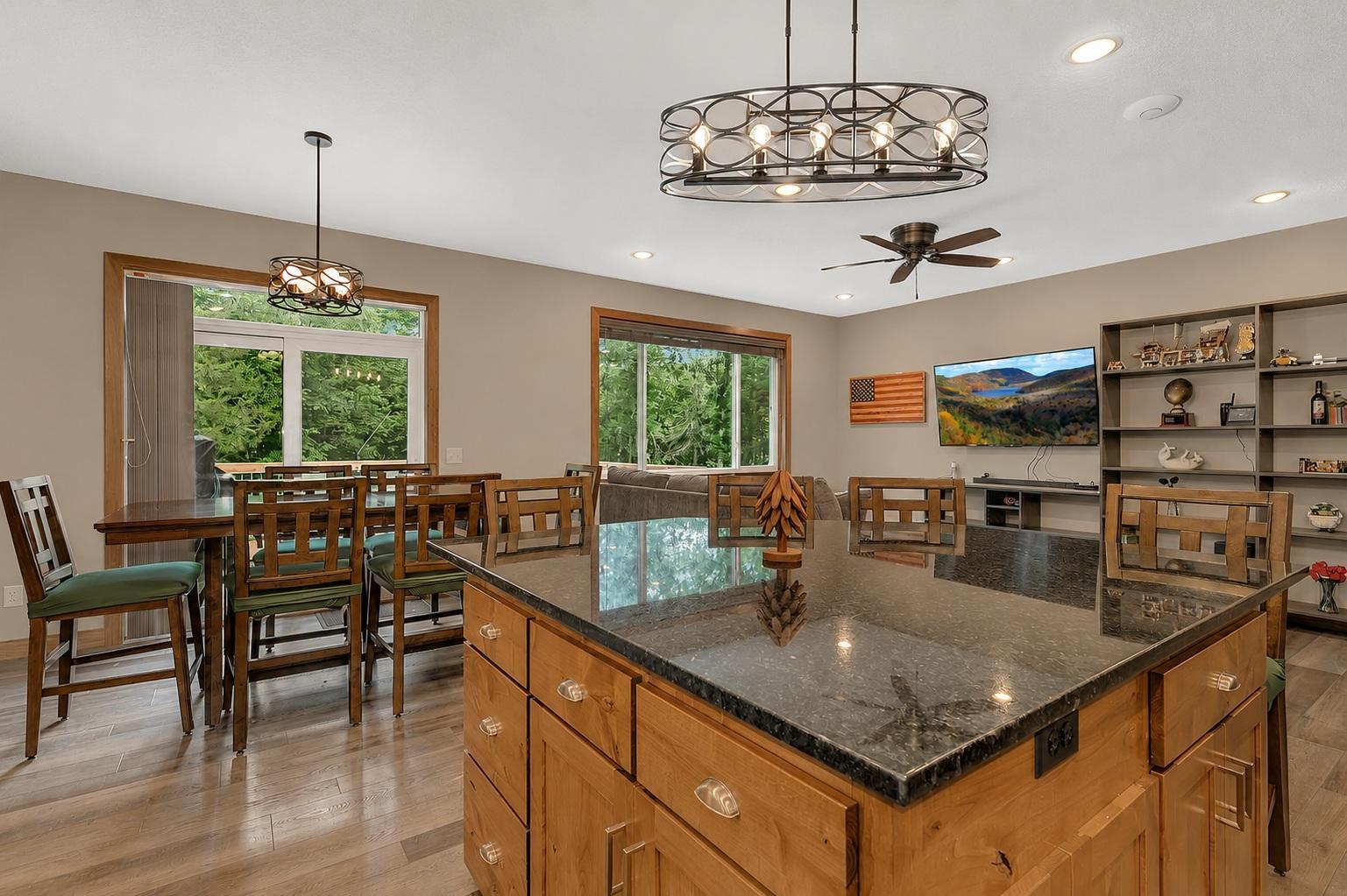 The kitchen features a center island, generous workspace, and seamless flow to the dining and living areas, while large windows fill the home with natural light and wooded views.