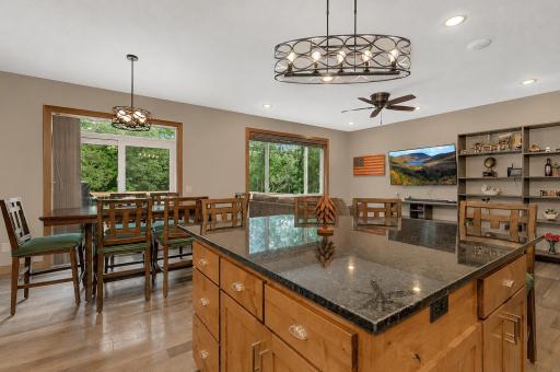 The kitchen features a center island, generous workspace, and seamless flow to the dining and living areas, while large windows fill the home with natural light and wooded views.