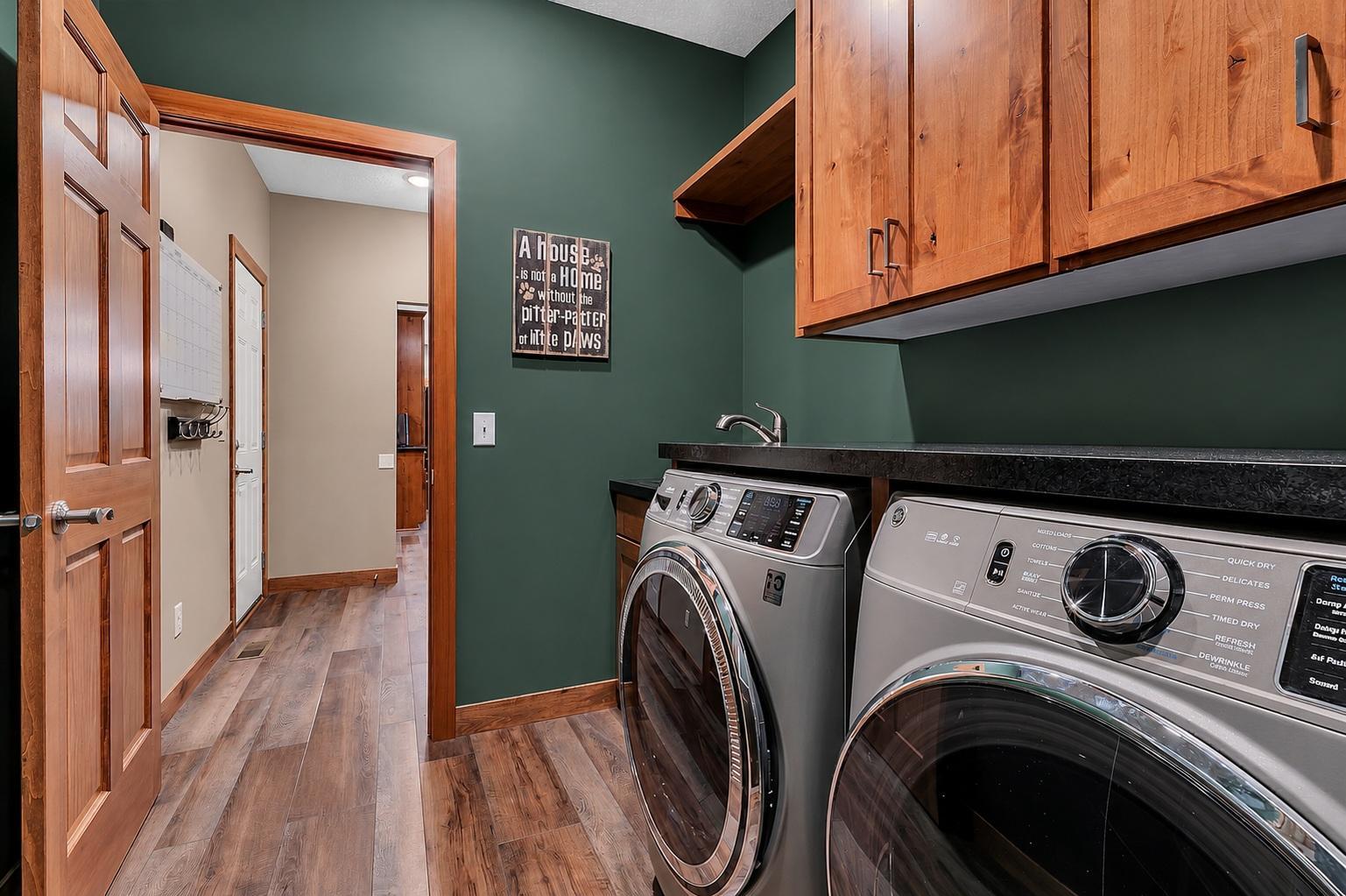 The centrally located laundry room connects the mudroom to the bonus room addition and includes a utility sink, abundant cabinetry, folding counter, and open shelving for added convenience.