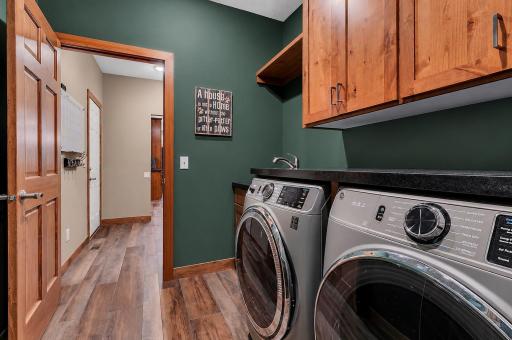 The centrally located laundry room connects the mudroom to the bonus room addition and includes a utility sink, abundant cabinetry, folding counter, and open shelving for added convenience.