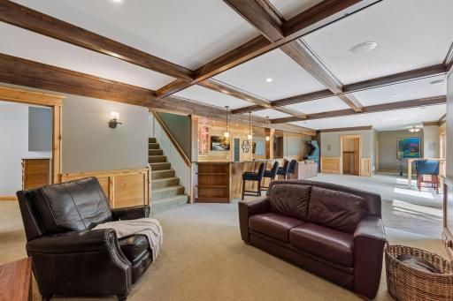 The perfect layout for hosting! This view shows how beautifully the lower level flows together, seamlessly connecting the cozy TV lounge & fireplace with the wet bar & the spacious open game area. Access the patio through the walkout patio door.