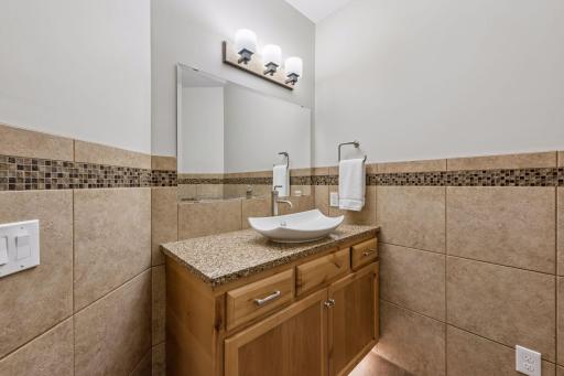 Perfect for guests! This convenient lower-level half bath is beautifully finished with durable ceramic tile floors and walls accented by sleek glass tile. It features a stylish vanity with plenty of storage, a Cambria countertop, and a vessel sink.