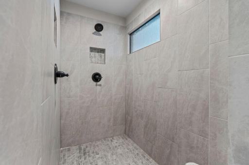 A gorgeous fully tiled shower with two shower heads and a transom window.