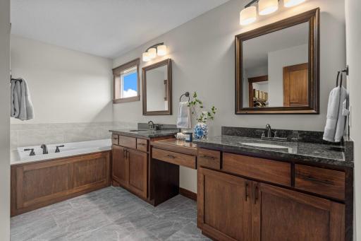 The primary bath boasts custom wood cabinets, independent vanities with granite counters, tile floors, and a soaking tub with tile surround. The transom window brings in natural light which is a rare feature in most bathrooms.