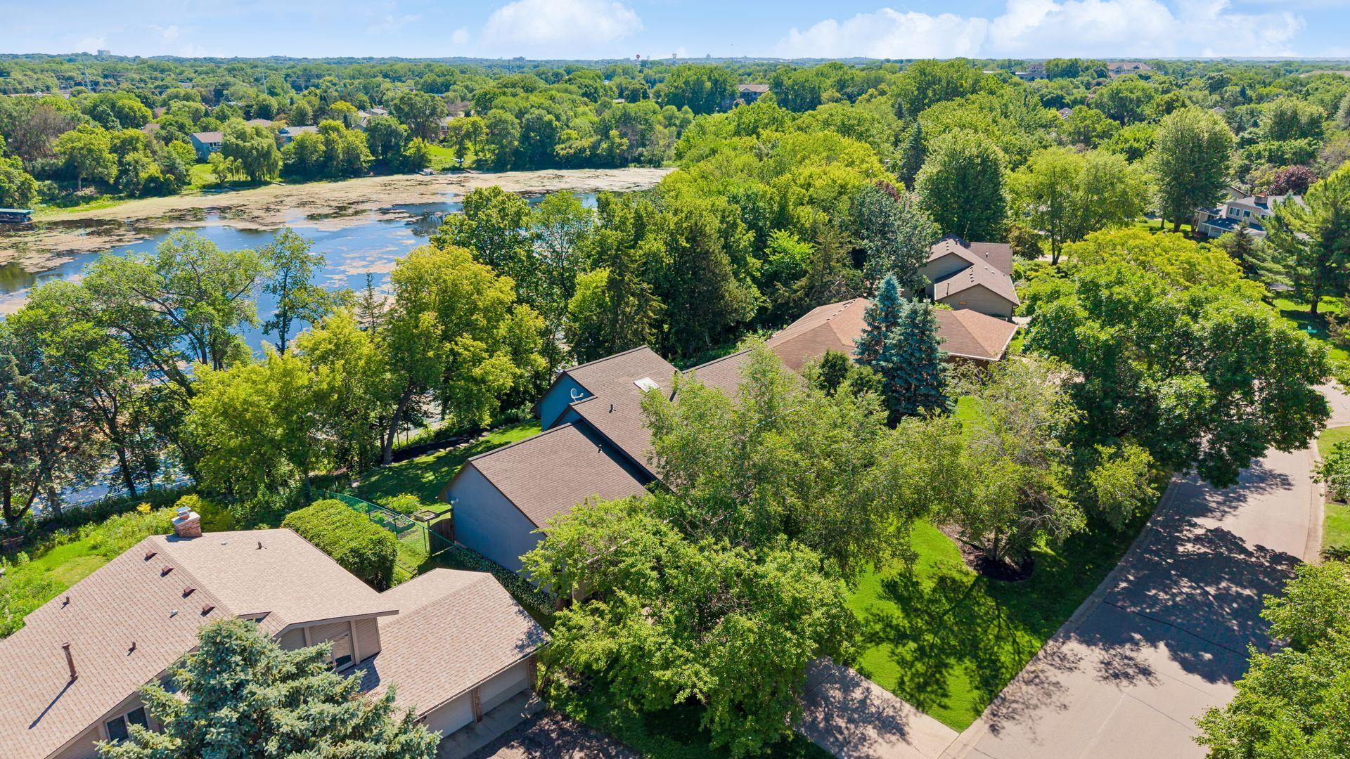 Aerial view of home with fenced backyard, mature trees for a private wooded feel, and Mitchell Lake in background.