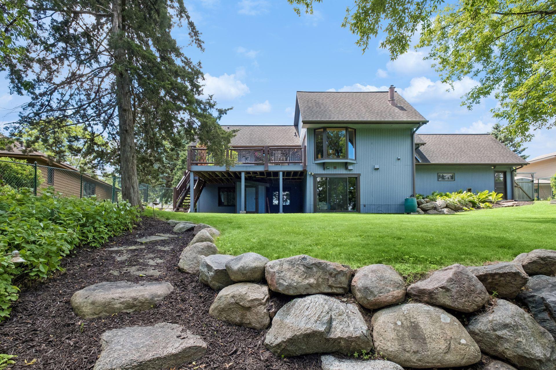 Natural stone pathway and boulder landscaping separate the grassy backyard from the firepit and dock areas.