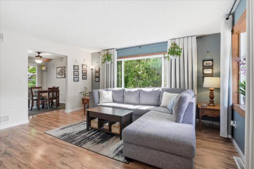 A large picture window serves as the focal point of the living room, framing scenic outdoor views while filling the space with sunlight. The neutral décor and generous seating area provide a warm and relaxing atmosphere.