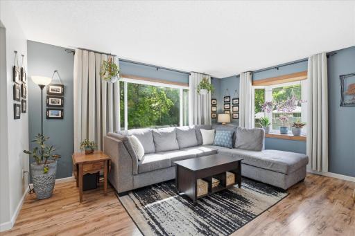 The spacious living room is filled with natural light from large picture windows overlooking mature greenery. Modern paint tones, updated flooring, and an open layout create a comfortable space for everyday living and entertaining.