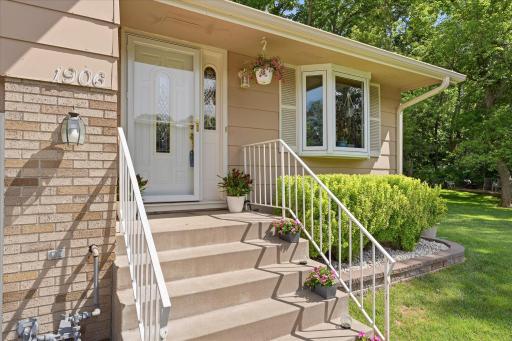 A charming front entrance welcomes guests with updated railings, decorative planters, and a covered landing. The bay window and landscaped garden bed enhance the home's inviting character.