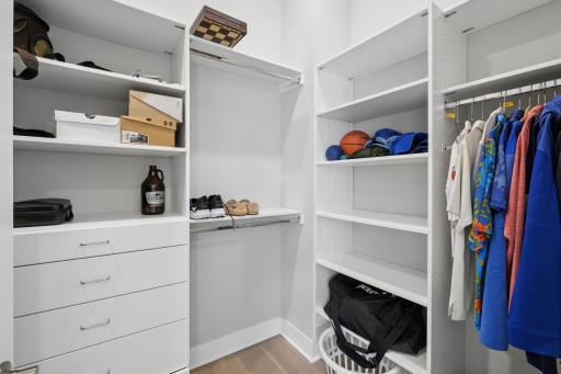 A spacious and thoughtfully designed primary walk-in closet offering both style and functionality. This well-organized space features custom built-in shelving, ample hanging areas for both long and short garments, and dedicated compartments for shoes
