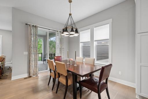 A casual dining area with windows and inviting light feels effortlessly warm and welcoming. Sunlight filters through wide panes of glass, casting soft, shifting patterns across a simple wooden table. Doors open to screened in porch.