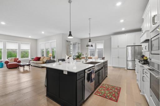 A spacious kitchen centered around a large island, stylish, comfortable with bar style seating. Ample workspace for cooking and baking. The smooth quartz countertops add a touch of elegance, ideal for everyday use. Pendant lights add a warm glow.