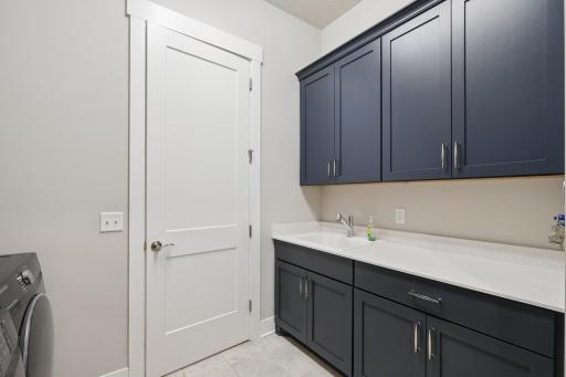 Surrounding the sink are sturdy cupboards that provide ample storage for cleaning supplies, detergents, and household items. The cabinetry is clean-lined, offering both upper and lower storage to keep the space organized and clutter-free.