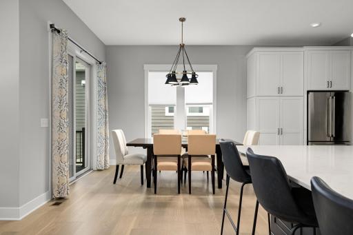 A casual dining area with windows and inviting light feels effortlessly warm and welcoming. Sunlight filters through wide panes of glass, casting soft, shifting patterns across a simple wooden table.
