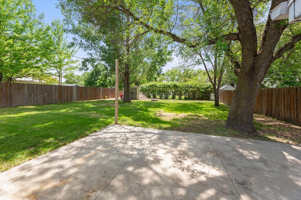 Fully fenced yard w/ lots of mature trees, concrete patio, & storage shed.