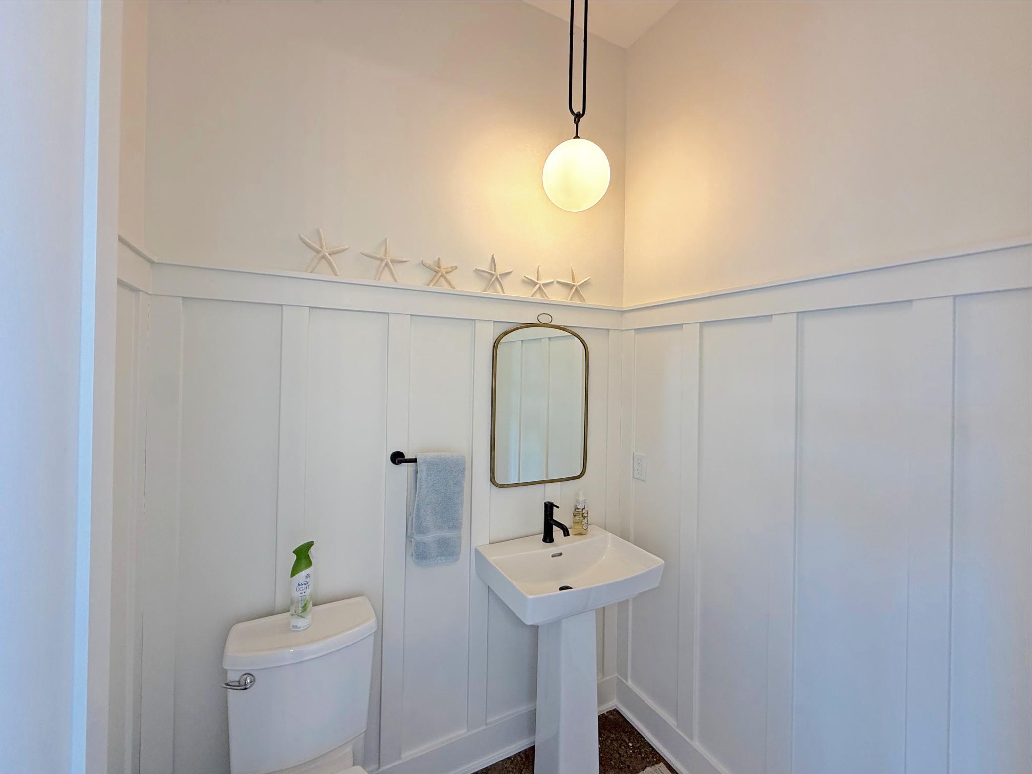 The main-level half bath is full of charm and character, featuring custom board-and-batten wall detailing, a stylish pedestal sink, and modern fixtures.