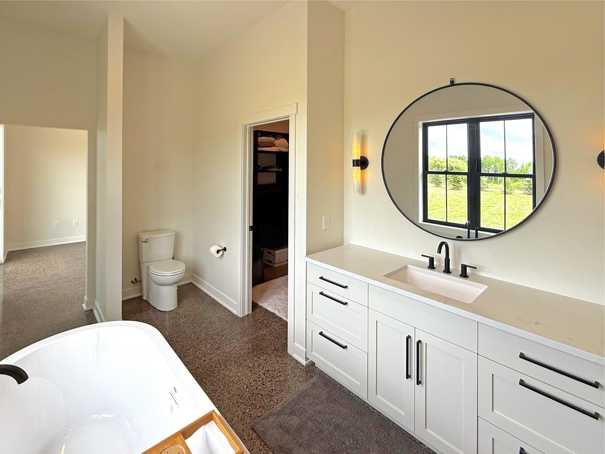 A custom vanity offers abundant storage, and a large round mirror creates a striking focal point. A spacious walk-in closet completes the space.