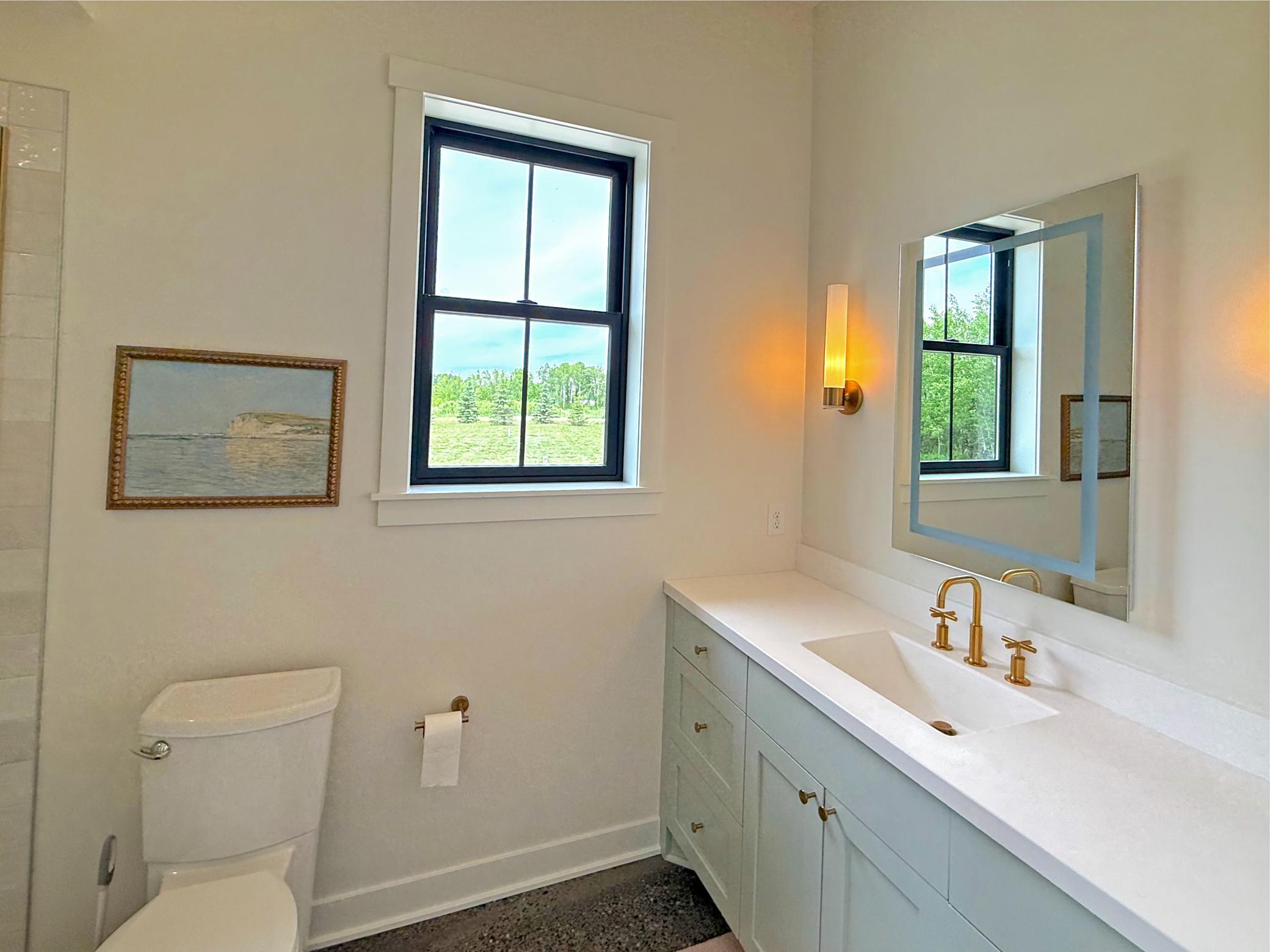 The well-appointed bath includes a tiled walk-in shower, custom vanity, and large window that fills the space with natural light, creating a bright retreat.