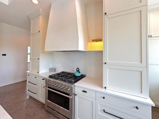 This gourmet kitchen is thoughtfully designed with custom cabinetry, high-end gas stove, and a striking custom range hood that serves as a centerpiece of the space.