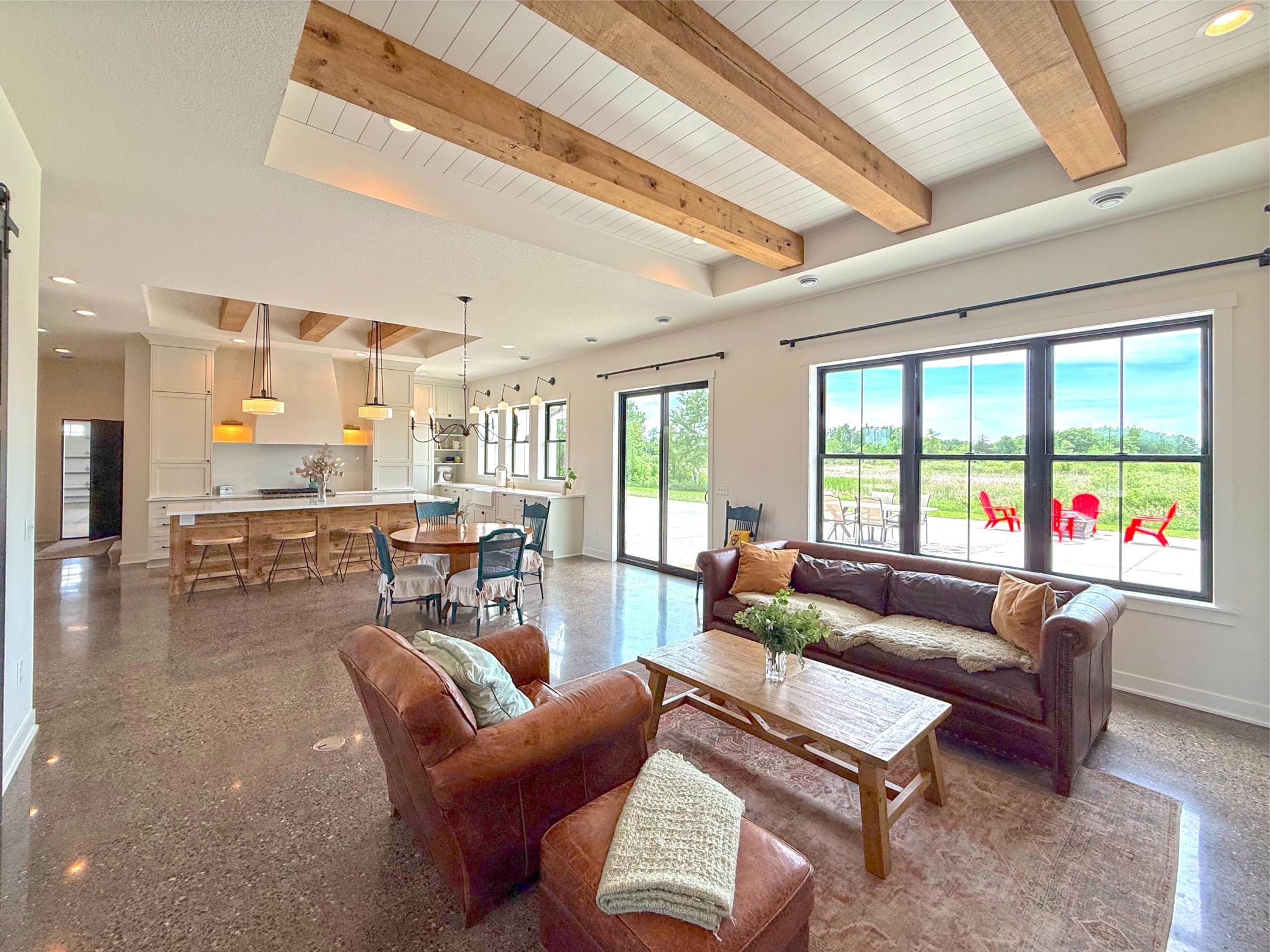 Reclaimed wood beams and beadboard ceiling details add character and architectural interest, while oversized windows frame picturesque country views