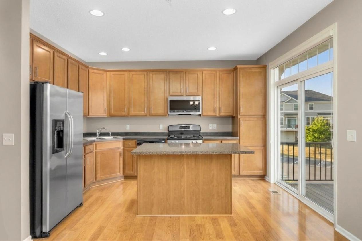 Functional and stylish kitchen with maple cabinetry, stainless steel appliances, center island, ample counter space, and direct access to the maintenance-free deck. New microwave 2025.