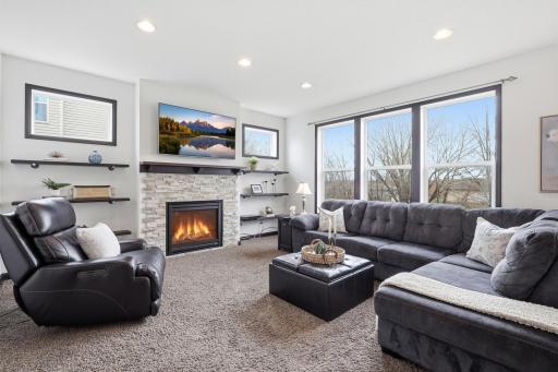 Spacious great room featuring a stunning stone surround gas fireplace, custom display shelving, and expansive windows that fill the home with natural light.