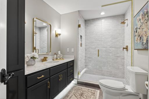 Stylishly updated bath featuring jewel tones, tiled shower, frameless glass doors, elegant mirror, and polished brass fixtures.