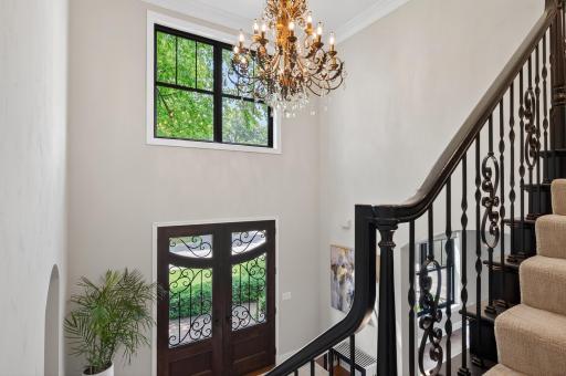 Dramatic two-story foyer with elegant wrought iron staircase and statement chandelier. Natural light pours through oversized windows, highlighting soaring ceilings and creating an unforgettable sense of arrival.