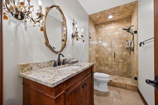 Elegantly finished full bath featuring natural stone tile, a glass-enclosed shower, and refined fixturesâoffering guests a spa-like experience within the lower level.