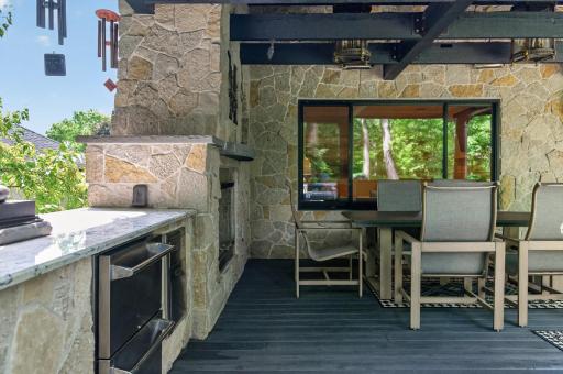 Inviting covered lounge centered around a striking stone fireplace, creating a warm and intimate setting enhanced by curated lighting and seamless indoor-outdoor flow.