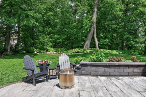 Charming patio retreat with built-in fire feature and seating areaâan ideal setting for evening gatherings surrounded by mature trees and tranquil landscaping.