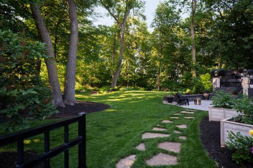 Expansive, park-like backyard with mature trees, open green space, and a natural, private settingâfeaturing a stone path and patio.