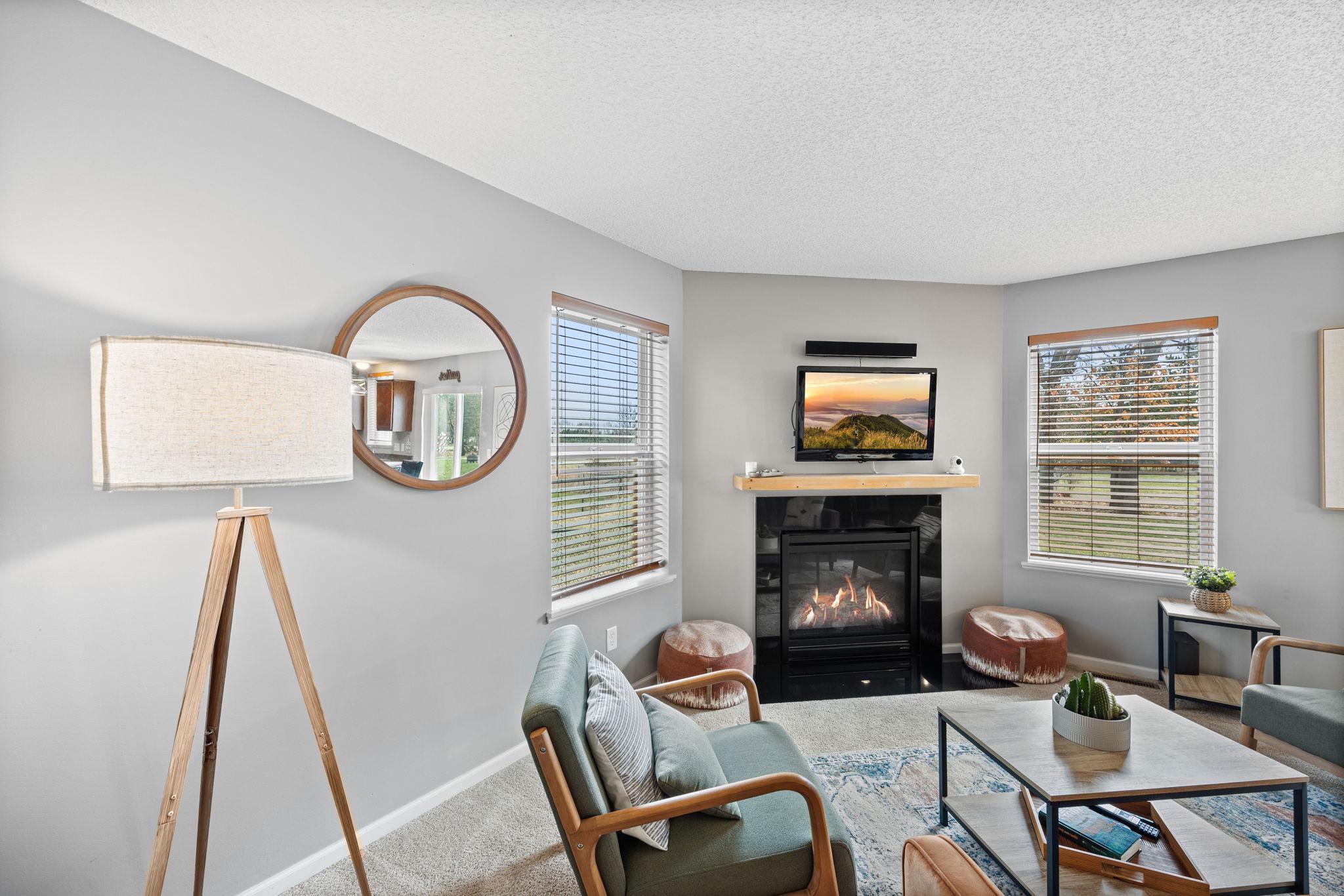 The living room feels comfortable and relaxed, featuring soft carpeting, a Heat-n-Glo fireplace, and large windows that bring in natural light and views of the backyard.