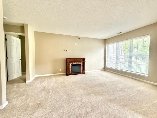 Living room space without furniture; electric fireplace can be moved to desired location. Entry to primary bedroom on the left.