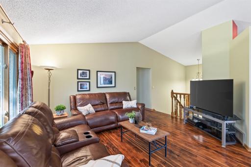 Large living room space with laminate wood flooring, vaulted ceiling.