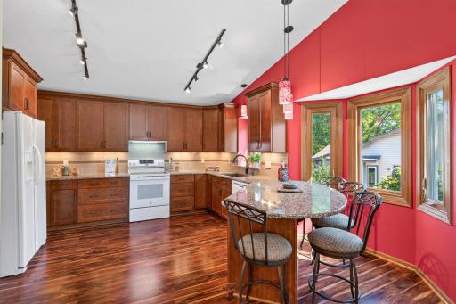 Beautifully updated kitchen w/vaulted ceiling, laminate wood flooring, cherry cabinets w/soft close drawers, undercounter lighting, Cambria countertops, track lighting, peninsula w/spacious 4 stool seating, bay window, brand NEW stove & drink fridge.