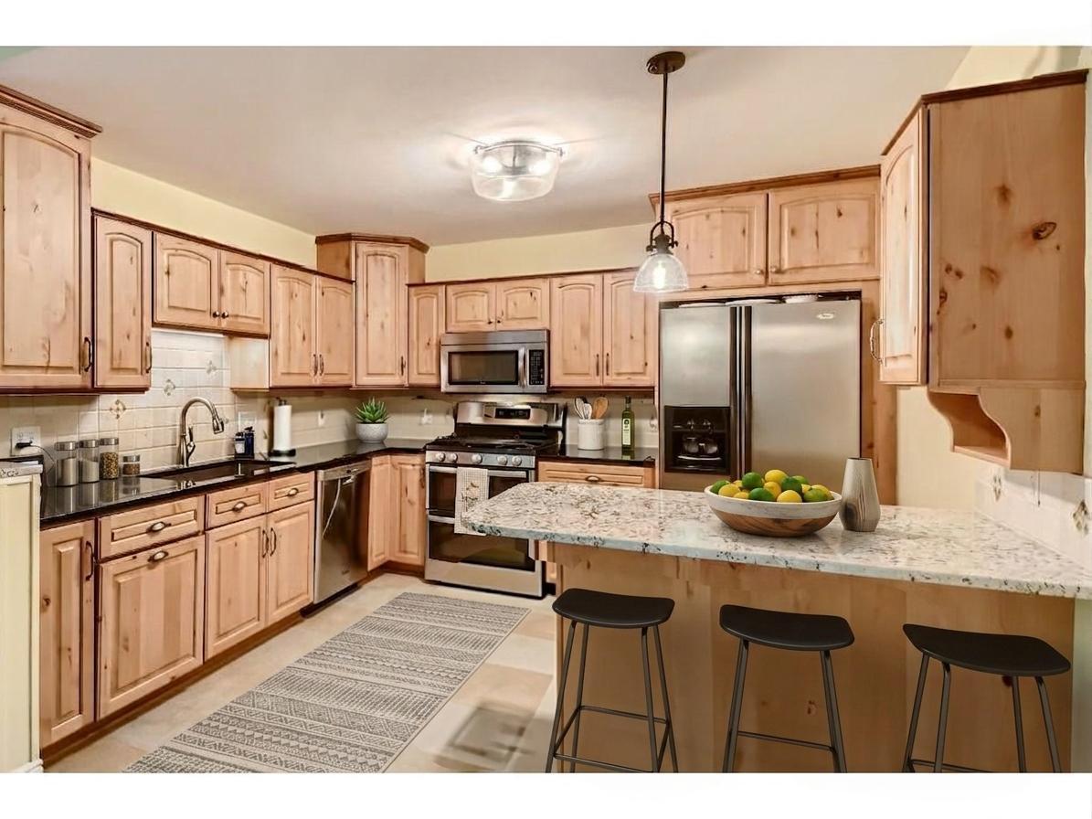 Bright kitchen featuring warm wood cabinetry, stainless steel appliances, and a functional L-shaped breakfast bar setup. Perfect for casual dining and prep! *Virtually staged to show design options.