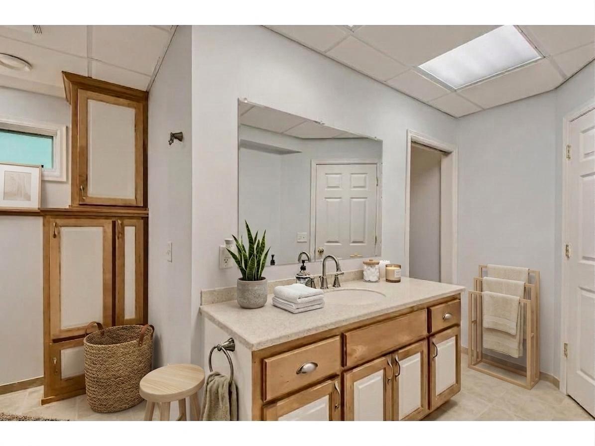 The lower-level bathroom features a wide vanity with ample drawer storage, matching built-in linen cabinetry, and bright mirror lighting! *Virtually staged to show design options.