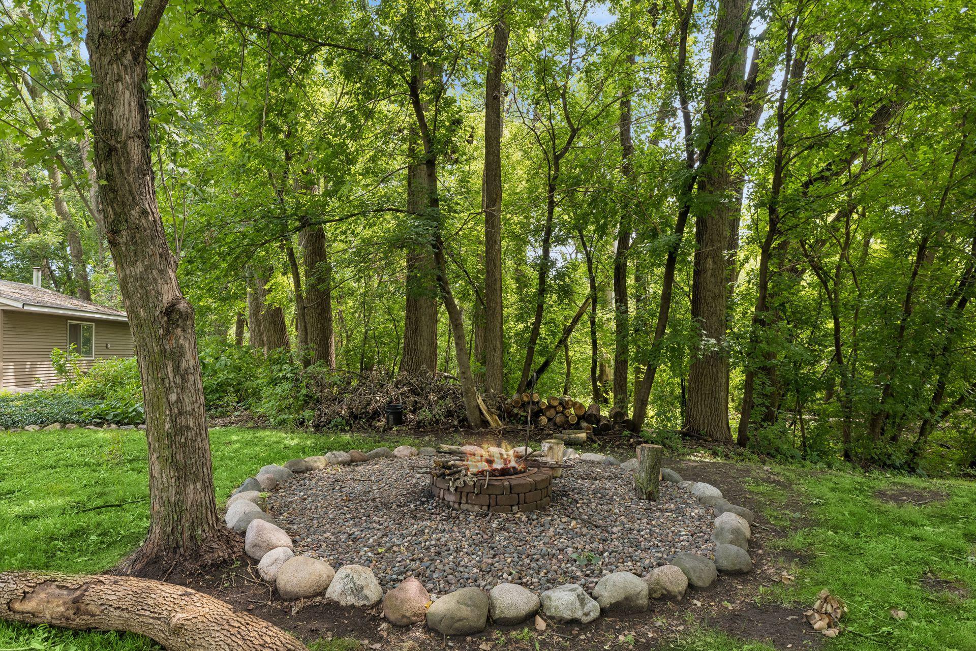 The private backyard oasis features a stone fire pit surrounded by mature trees. Perfect for relaxing and outdoor gatherings!
