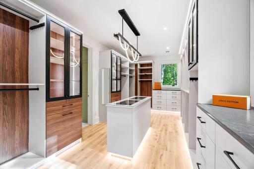 Luxurious custom walk-in closet featuring illuminated display cabinetry, a center storage island, built-in organization systems, and designer lighting