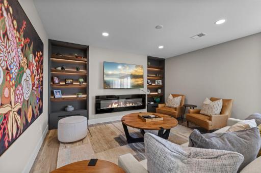 Large family room showcasing a cozy, electric fireplace, a wall of custom built-ins, floating shelving, accent lighting.