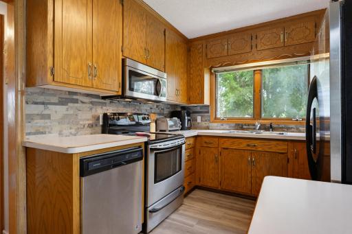 The kitchen features laminate countertops, LVP flooring, a stone backsplash, and a suite of S.S. appliances including a dishwasher, microwave, refrigerator, and and electric range.