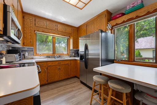 The kitchen features laminate countertops, LVP flooring, a stone backsplash, and a suite of S.S. appliances including a dishwasher, microwave, refrigerator, and and electric range.