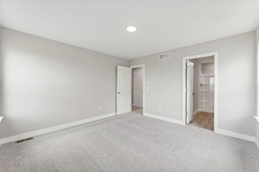 In this view of the primary bedroom you can see the en-suite bathroom. There is also a walk-in closet just beyond the bathroom door. Photo of spec home, colors and finishes will vary.
