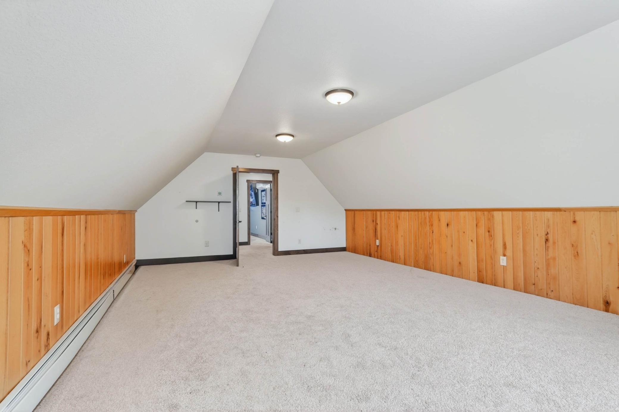 Large upper-level bonus room with sloped ceilings, wood wainscoting, and flexible space for recreation, guests, hobbies, or a third living area.