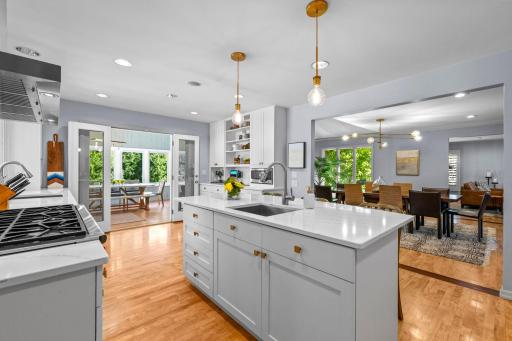 Gourmet kitchen featuring abundant HanStone quartz countertops, pristine white cabinetry, a spacious center island with breakfast bar seating, and elegant gold LED pendant lighting.