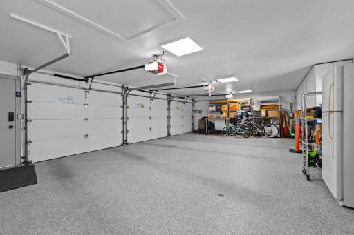The oversized heated three-car garage, which includes epoxy flooring, smart garage door openers with app-based controls, a mini-split heating and cooling system (2024), and abundant storage space.